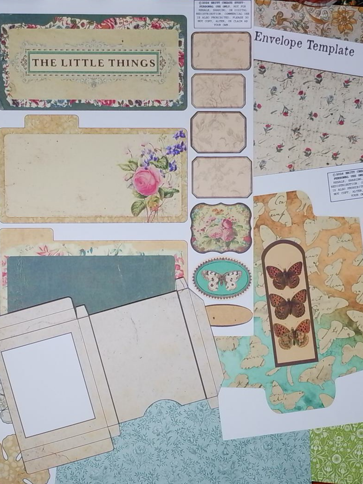 A flat lay of vintage-style scrapbook paper and envelope template pieces with floral, butterfly, and damask patterns in muted beige, green, pink, and blue tones.