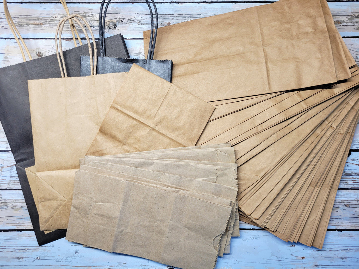 A bulk assortment of brown kraft paper shopping bags and gift bags, including some with black handles, arranged on a light blue distressed wooden surface.